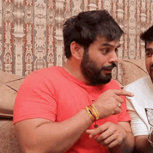 a man with a beard in a red shirt is pointing