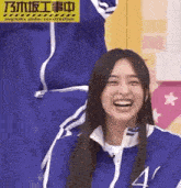 a woman in a blue jacket is smiling and laughing while sitting on a chair .