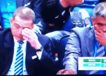 a man in a suit and tie wipes his nose while sitting in a stadium