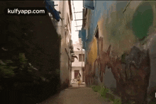 a person is walking down a narrow alleyway between two buildings with graffiti on the walls .