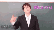 a man in a suit and tie stands in front of a blackboard with today 's topic written on it