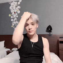 a man in a black tank top is sitting on a bed and touching his hair
