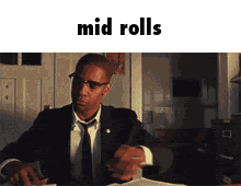 a man in a suit and tie is sitting at a desk with the words mid rolls written above him