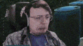 a man wearing headphones and glasses is sitting in a chair and looking at the camera .