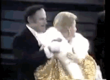 a man in a tuxedo is holding a woman in a fur coat while they are dancing .