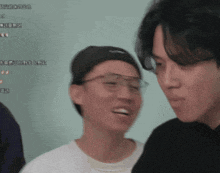 a man wearing glasses and a black hat looks at another man