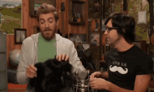 a man wearing a viva la mustache shirt holds a black cat