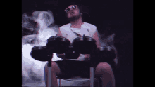 a man wearing sunglasses is playing drums in a dark room with smoke coming out of it .
