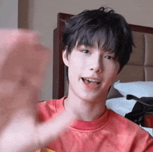a young man in a red tie dye shirt is waving at the camera