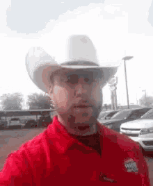 a man wearing a red shirt and a cowboy hat is taking a selfie .