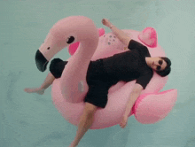 a man is laying on a pink flamingo float in the water