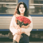 a young woman is holding a bouquet of red roses .