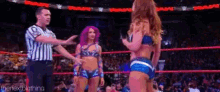 a referee is standing next to two women in a wrestling ring during a match .