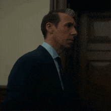 a man in a suit and tie stands in front of a door that says ' e ' on it