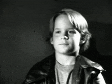 a black and white photo of a young boy wearing a leather jacket and smiling