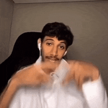 a man with a mustache is sitting in a chair wearing ear buds and a white shirt .