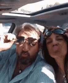 a man and a woman are sitting in a car and the woman is blowing a kiss