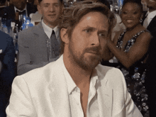 a man with a beard wearing a white suit looks at the camera