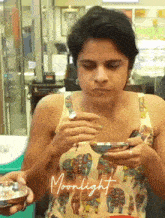 a woman in a tank top with elephants on it is eating something from a bowl
