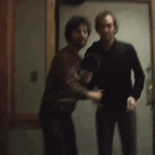 a blurry picture of two men standing next to each other in a doorway .