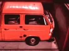 a red van is sitting on top of a tow truck in a dark room .