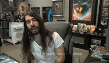 a man with long hair and a beard is sitting in front of a computer screen that says artificialshenanians