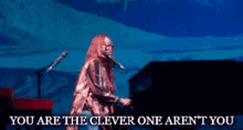 a woman singing into a microphone with the words you are the clever one aren 't you below her