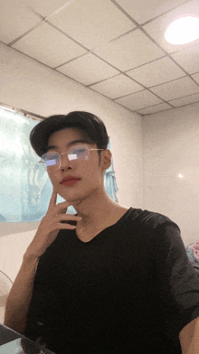 a young man wearing glasses and a black shirt is touching his chin