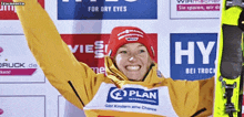 a woman wearing a yellow jacket and a red hat holds up her arms in front of a sign that says hy