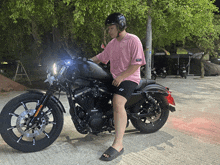 a man in a pink shirt is standing next to a black motorcycle