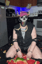 a man wearing a skull mask is sitting on the floor with watermelon