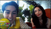 a man and a woman are sitting next to each other in front of a screen that says " want "