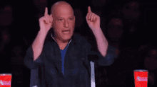 a bald man is giving the middle finger while sitting in front of a microphone in front of a dunkin donuts cup .