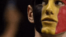 a man with red yellow and black paint on his face looks at the camera
