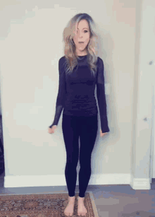 a woman in a purple shirt and black pants is standing on a rug .