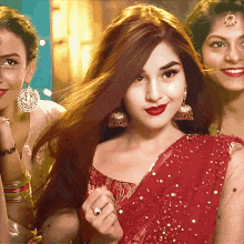 three women are posing for a picture and one is wearing a red saree