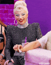 a woman in a black and white polka dot dress is sitting next to a pink cake and smiling .