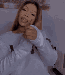a woman in a white sweater is giving a thumbs up sign
