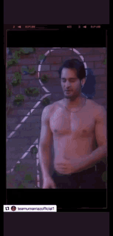 a shirtless man standing in front of a brick wall
