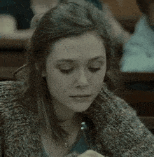 a woman wearing a sweater is sitting in a classroom