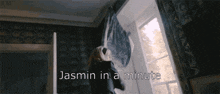 a woman throws a pillow in front of a window with the words jasmin in a minute written below her