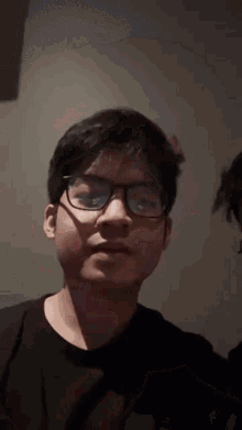 a young man wearing glasses and a black shirt is making a face .