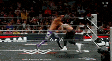 two men are wrestling in a ring with a crowd watching . one of the men has the number 87 on his shirt .