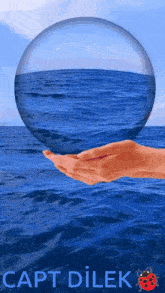 a hand is holding a glass ball over the ocean with the caption capt dilek