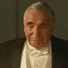 an older man in a tuxedo and bow tie is making a sad face .