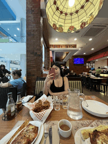 a woman sits at a table in a restaurant taking a selfie