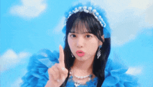a girl wearing a blue dress and pearls is pointing upwards