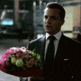 a man in a suit and tie holding a bouquet of pink flowers