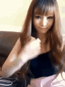 a woman with long hair is sitting on a couch and holding her fist up .