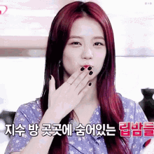 a woman with red hair and black nails is blowing a kiss with her hand .